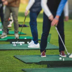 Group of golfers practicing and training golf swing on driving range practice, men playing on golf course, golf ball at golfing complex club resort, summer sunny day